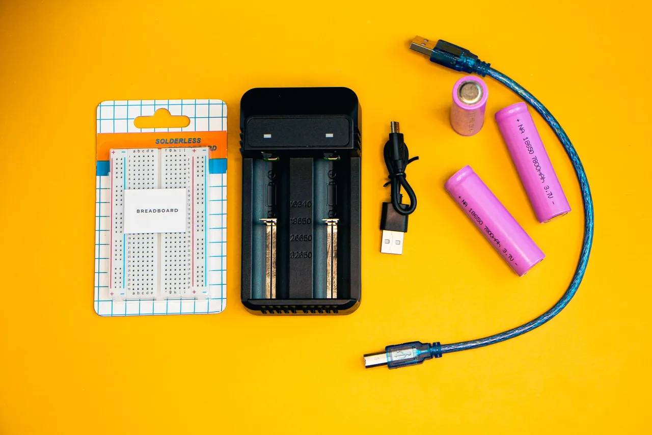 Flat lay of electronics including a breadboard and battery charger against a vibrant yellow backdrop.