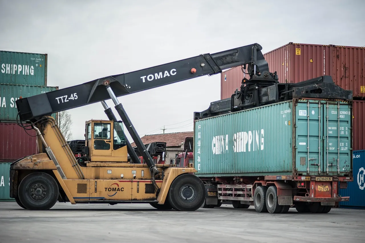 Container handler lifting a shipping container at a busy port terminal.