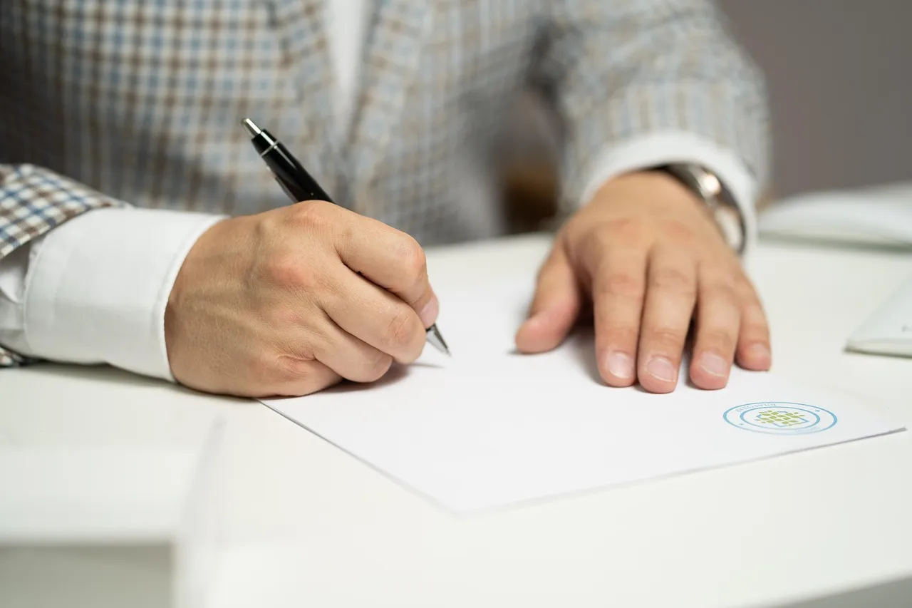 A man signing a paper document at a desk.